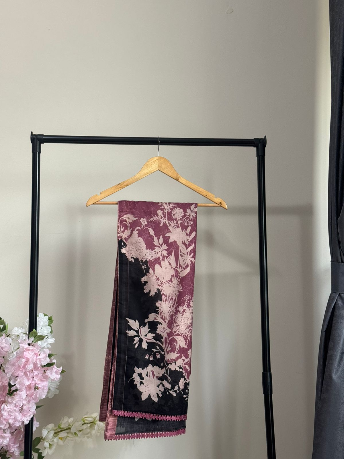 Decorative scarf with floral pattern hanging on a rack against a neutral wall.