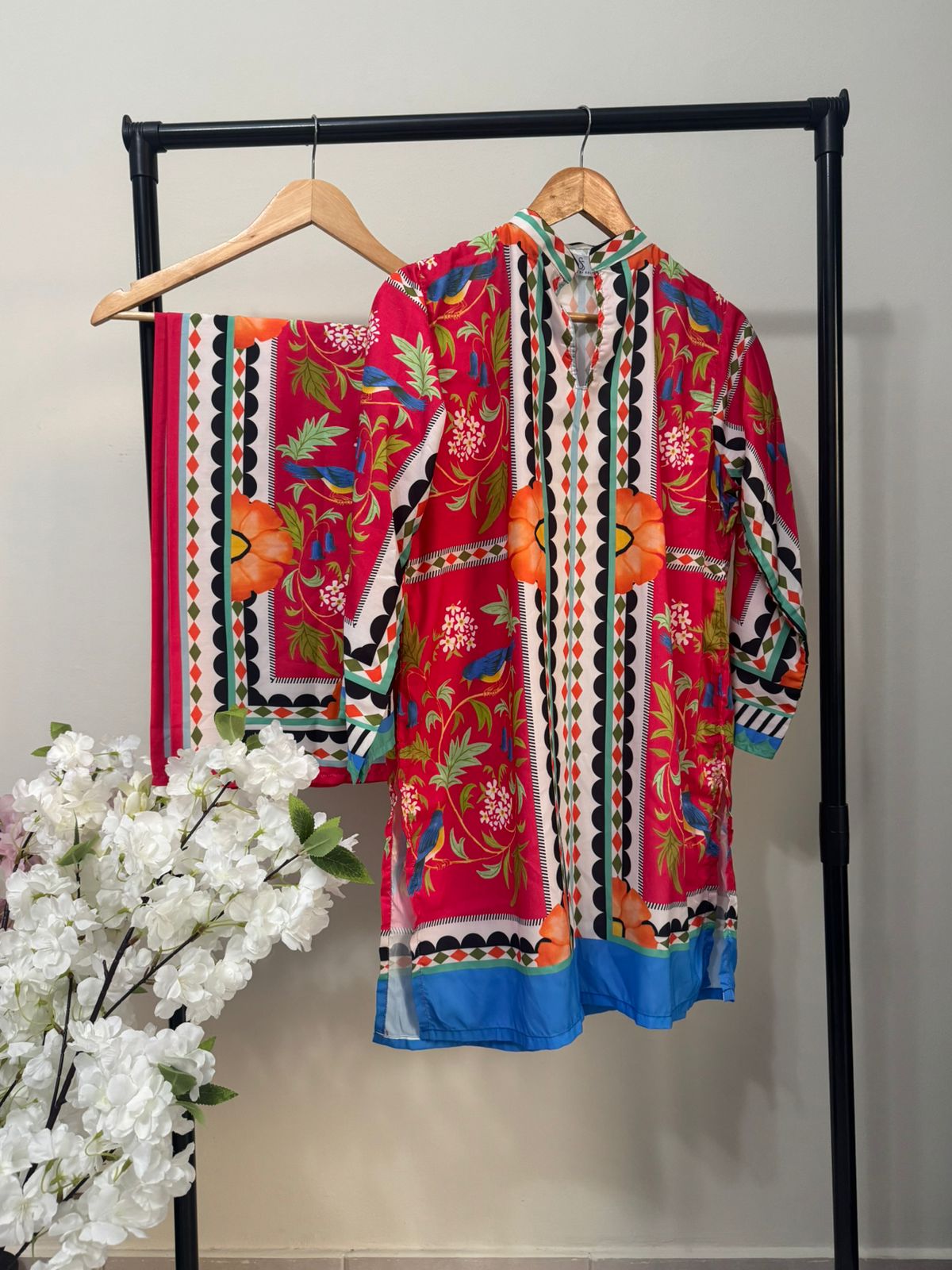 Colorful embroidered shirts on a rack with white flowers in the foreground