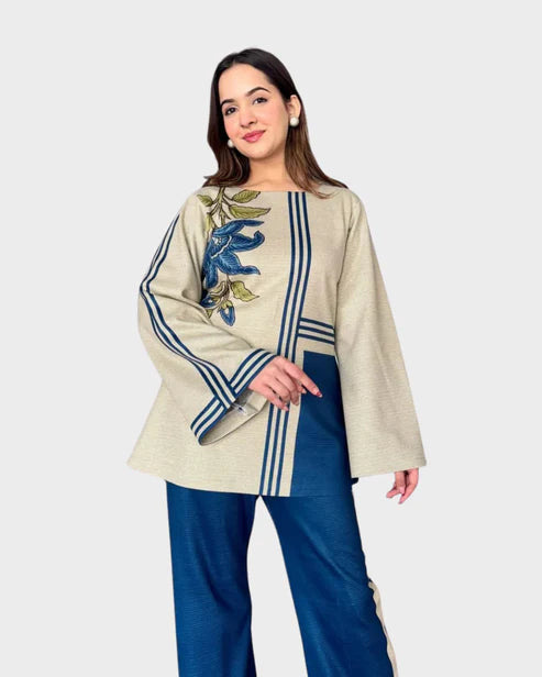 Woman wearing a beige top with floral embroidery and blue pants on a white background