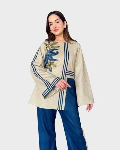 Woman wearing a beige top with floral embroidery and blue pants on a white background