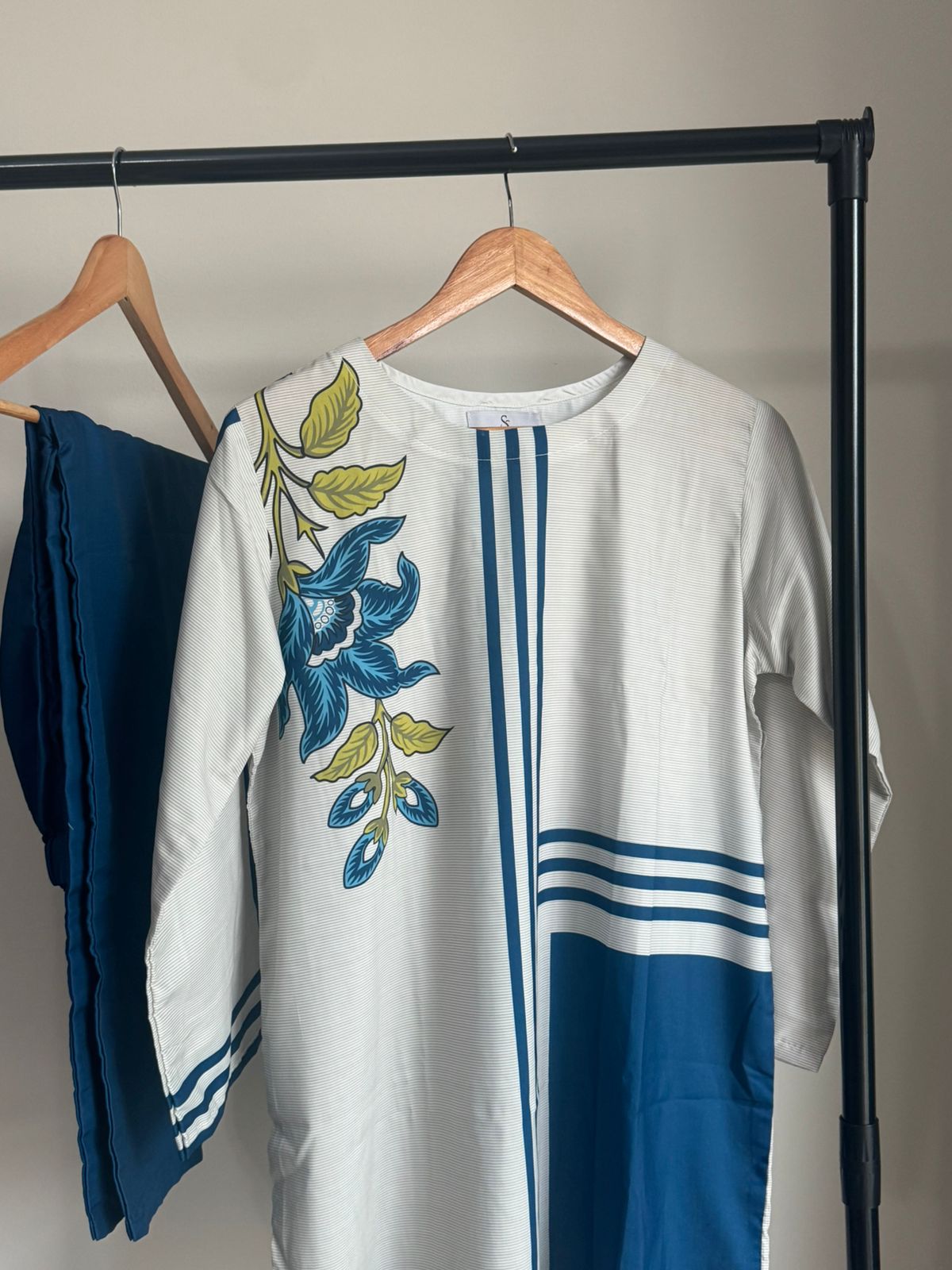 White shirt with blue floral embroidery on a hanger against a neutral background