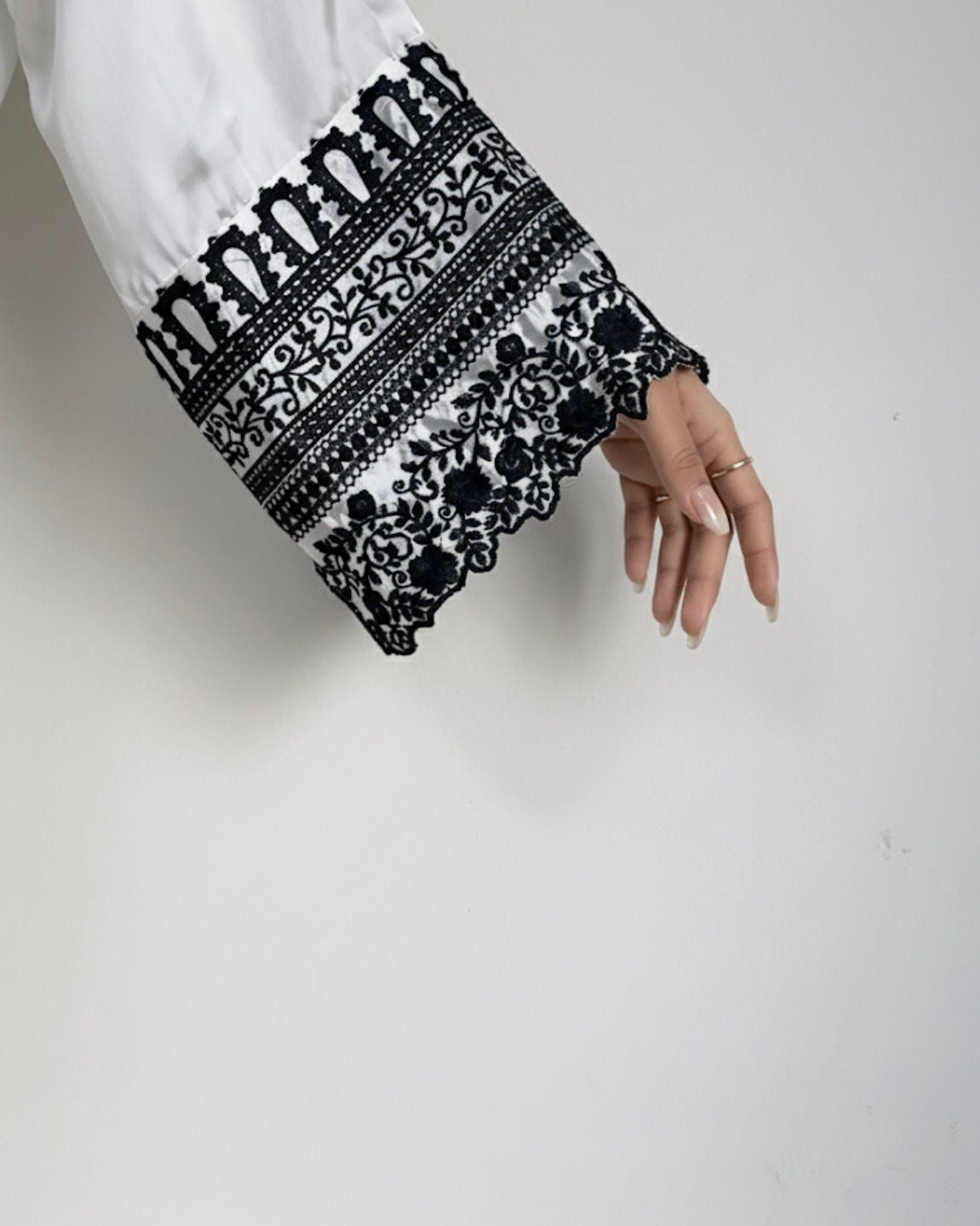 Close-up of a hand wearing a black and white embroidered sleeve against a plain background