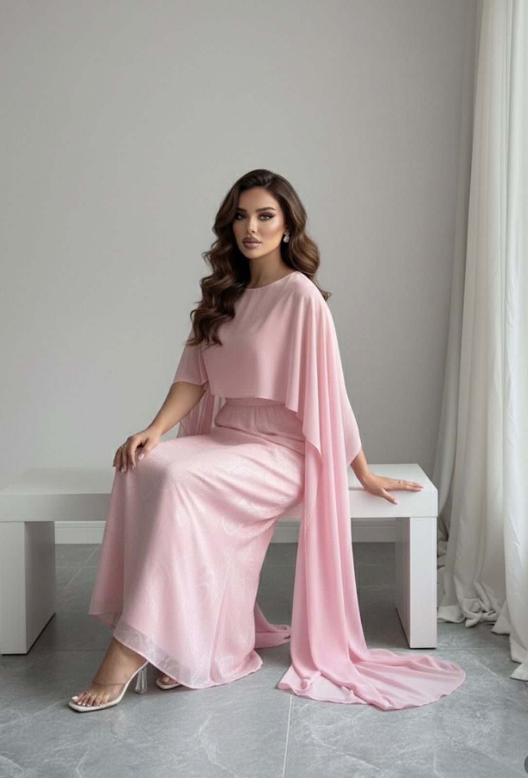 Woman in a pink dress sitting on a white bench against a gray wall.