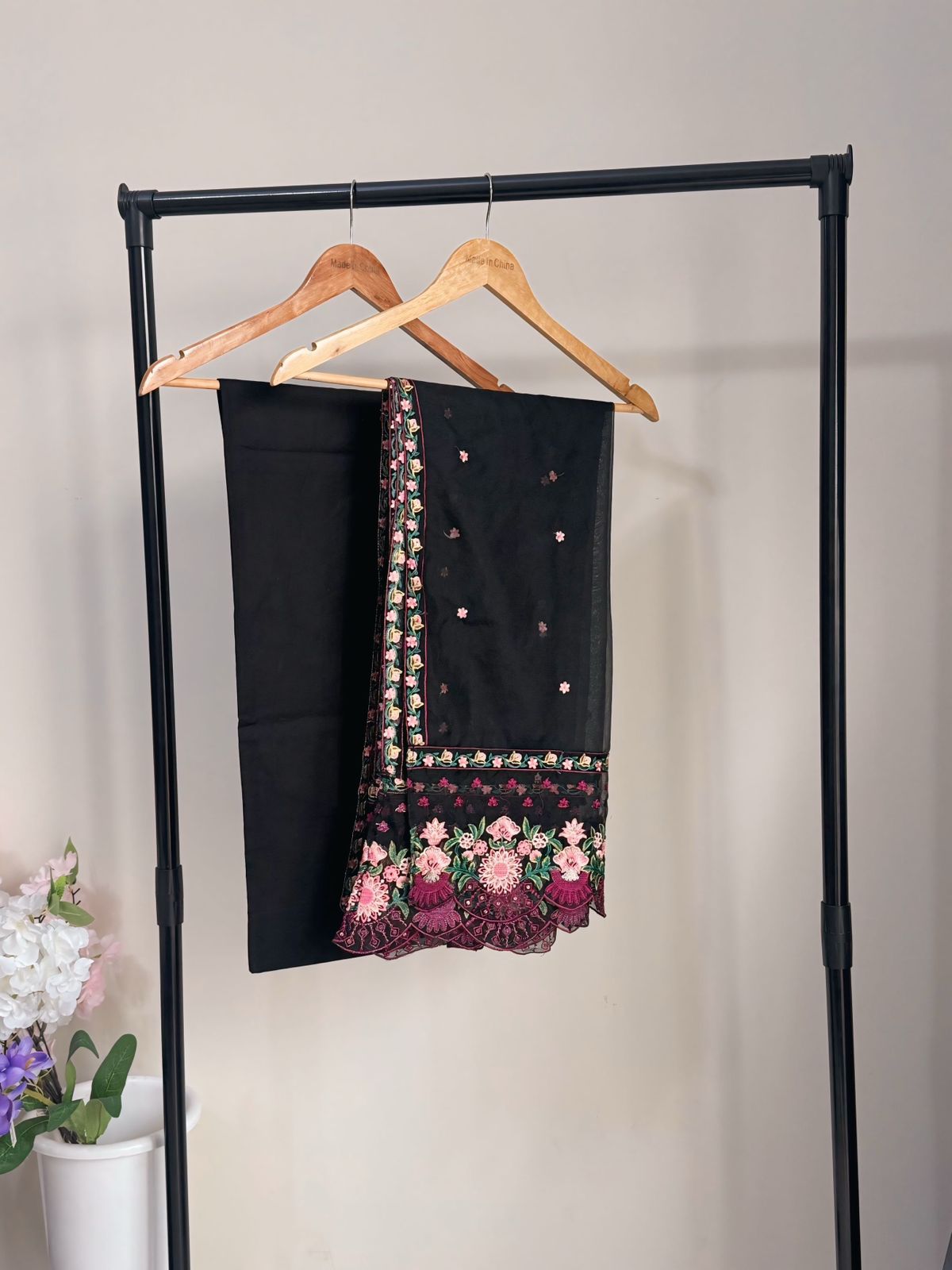Black scarf with floral embroidery on a hanger against a plain background
