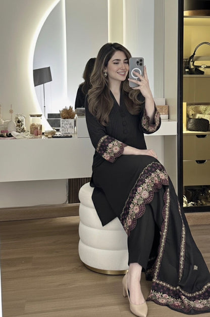 Woman in a stylish black outfit with floral patterns taking a selfie in a modern room.