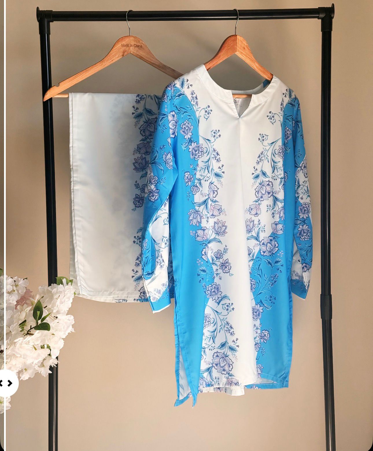 Blue and white floral dress on a hanger against a beige wall