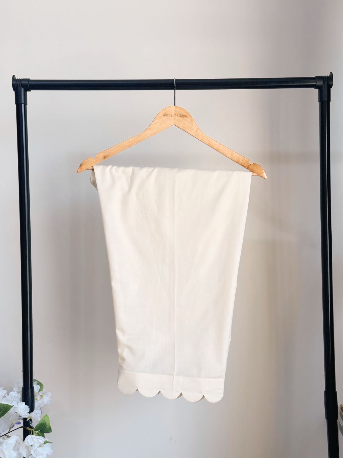 White scalloped skirt hanging on a wooden hanger against a plain background
