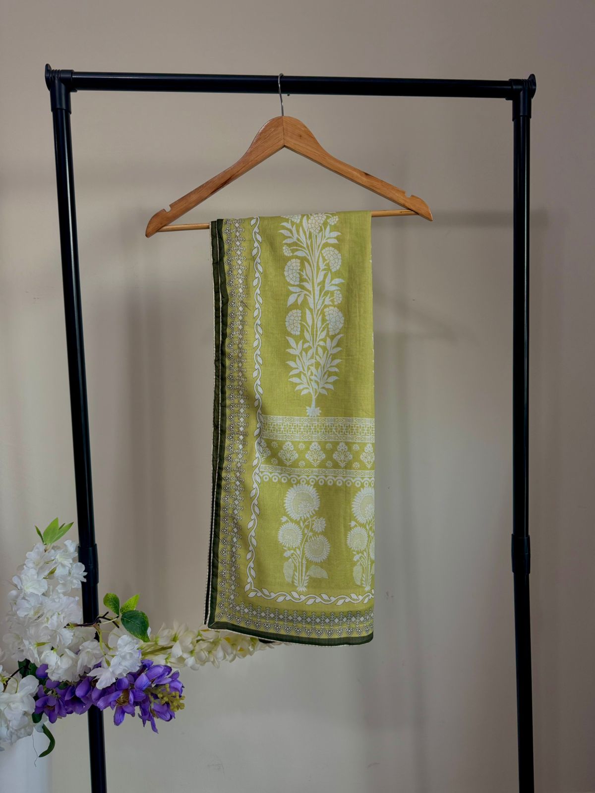 Green and white patterned scarf on a wooden hanger against a neutral background
