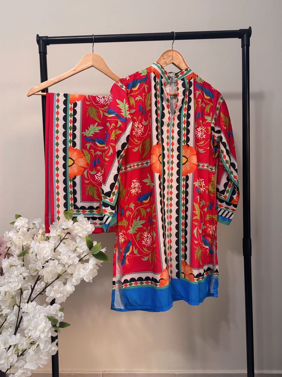 Colorful embroidered garment on a rack with white flowers in the foreground